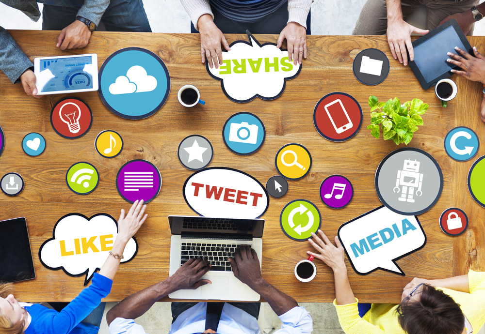 Group of people sitting around the table with scattered social logo paper cutouts.